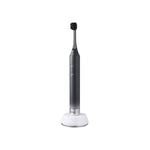 A sleek electric toothbrush with a dark gray handle and black bristles, resting on a white charging base against a solid white background. | Oral Care | YAMAN International